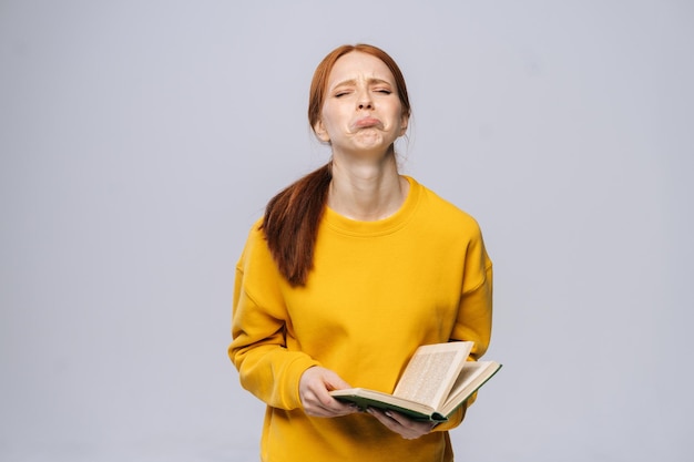 Crying unhappy young woman with closed eyes college student wearing yellow sweater holding book