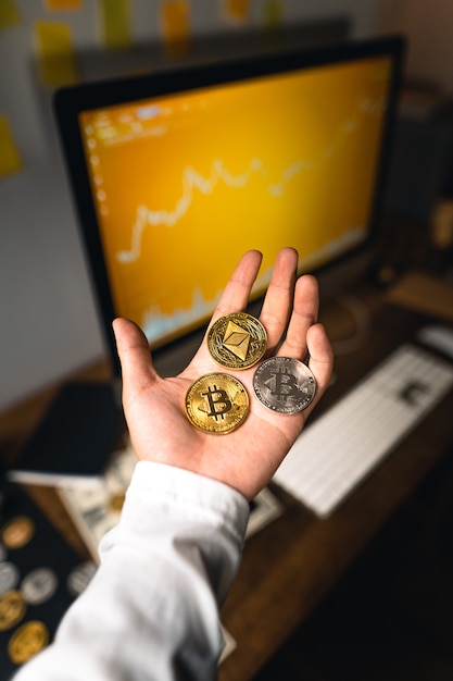 Photo the crypto in the hand in front of the desk and on the computer graph.