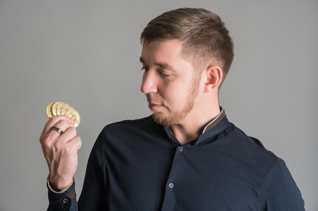 Crypto-investeerder die veel gouden btc-munten in zijn hand houdt die op een grijze achtergrond staan