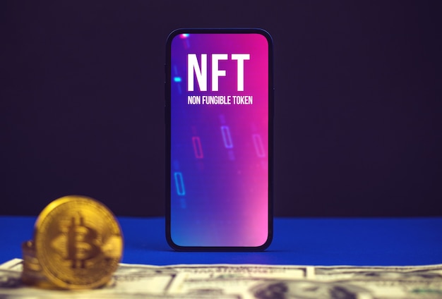 Криптоискусство и криптография, логотип токена NFT на экране современного мобильного телефона, офисный стол с долларом и криптовалютой биткойнами