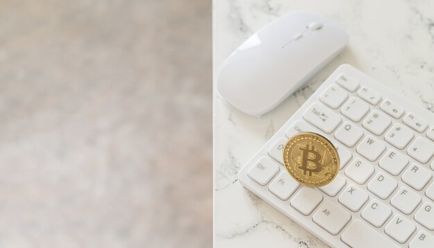 Cryptocurrency gouden bitcoin op wit computertoetsenbord naast muis op marmeren tafel