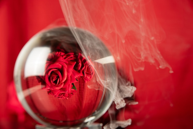 Crystal ball reflecting a bouquet of red roses and smoke, selective focus.