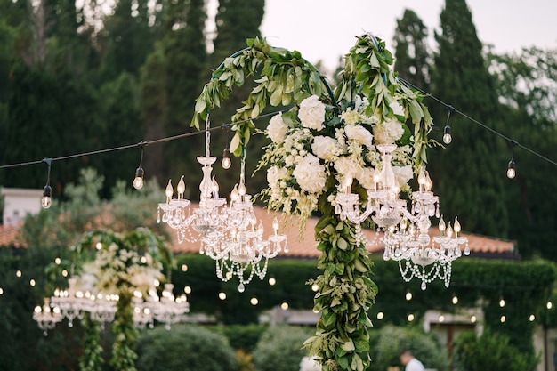 Crystal chandeliers and garlands decorate the wedding dinner outside among the trees