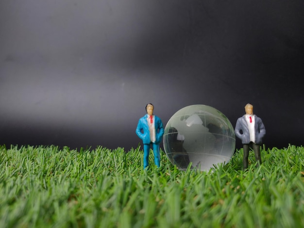 Crystal earth globe with miniature people on a grass background with copy space