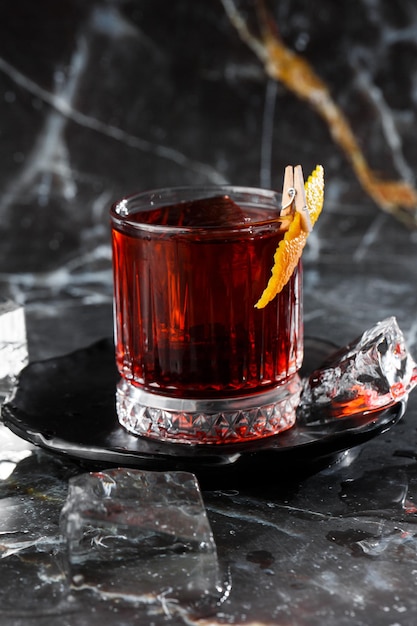 Foto bicchiere di cristallo con cocktail alcolico freddo brillante decorato con scorza d'arancia sfondo sfocato cocktail negroni