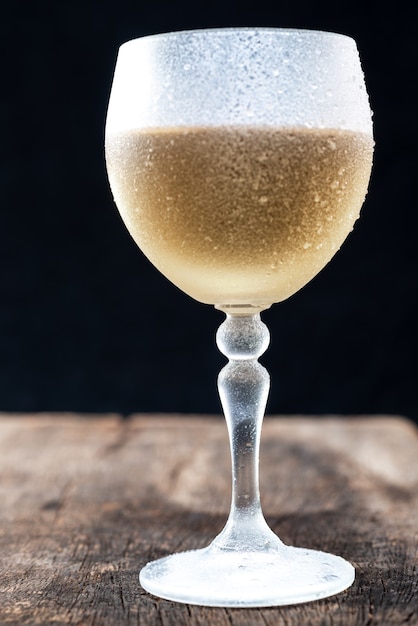Foto bicchiere di cristallo con vino bianco servito molto freddo, su un tavolo rustico con sfondo nero.