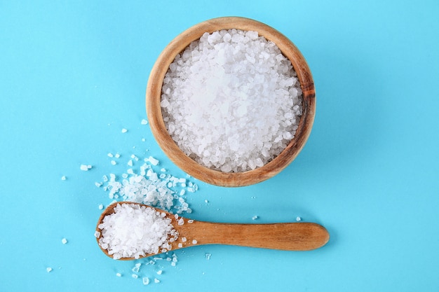 Crystals of large sea salt in a wooden bowl and spoon on a blue table.