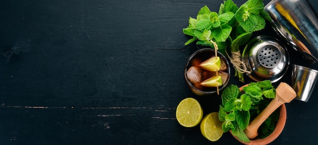 Cuba libre cocktail glass Lime mint On a black wooden background Free space for text