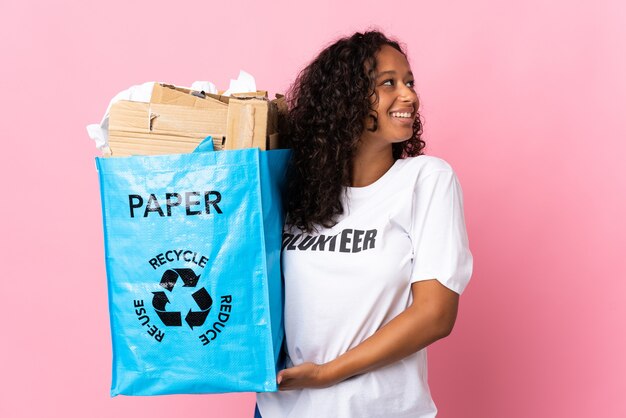 Cubaanse vrouw met een recycling zak vol papier om te recyclen geïsoleerd op roze uitziende kant
