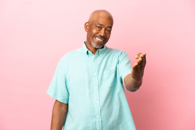 Cuban senior isolated on pink background shaking hands for closing a good deal