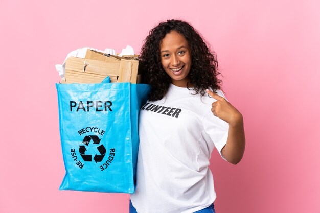 Cuban woman holding a recycling bag full of paper to recycle isolated on pink giving a thumbs up gesture