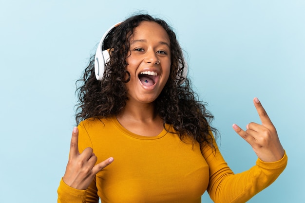 Cuban woman isolated on blue listening music making rock gesture