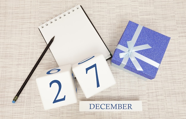 Cube calendar for December 27 and gift box, near a notebook with a pencil