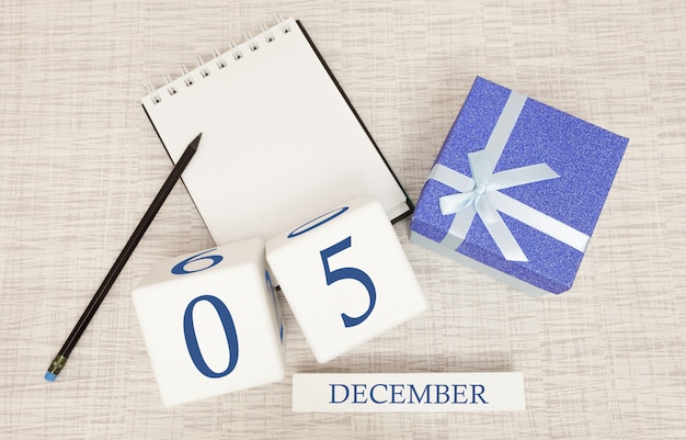 Кубический календарь на 5 декабря и подарочная коробка, рядом блокнот с карандашом