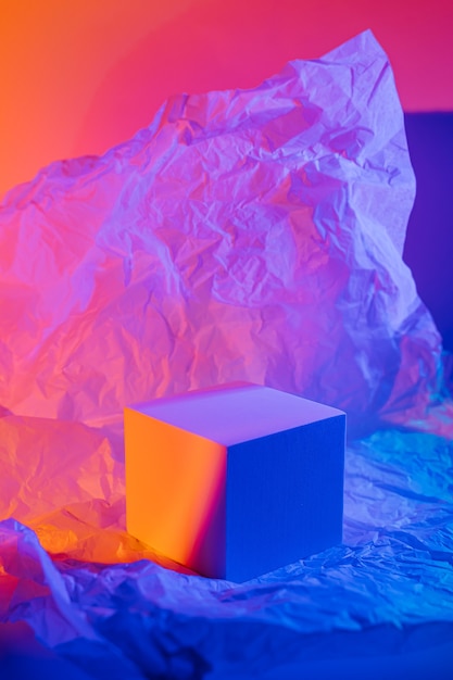 Cube podium with crumpled paper in neon light. stylish
geometric shapes to show products. abstract background