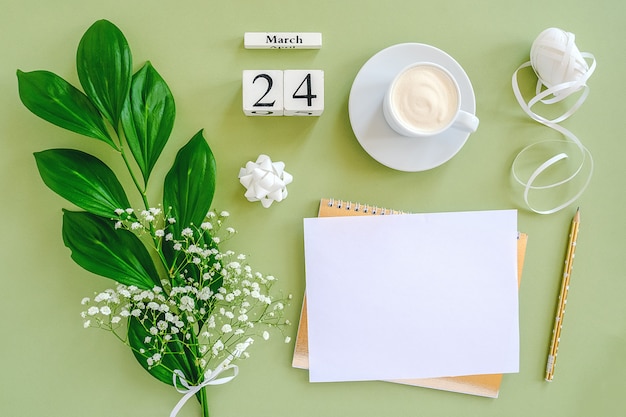 cubes calendar March 24. Notepad, cup of coffee, bouquet flowers on green background.