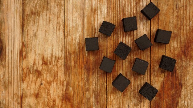 Photo cubes of coconut coal for hookah on wooden background. top view, place for text