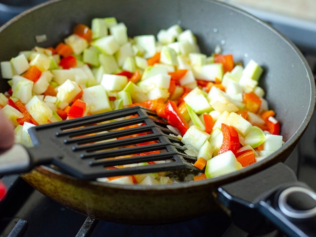 Cubes of fresh vegetables are fried in pan. 