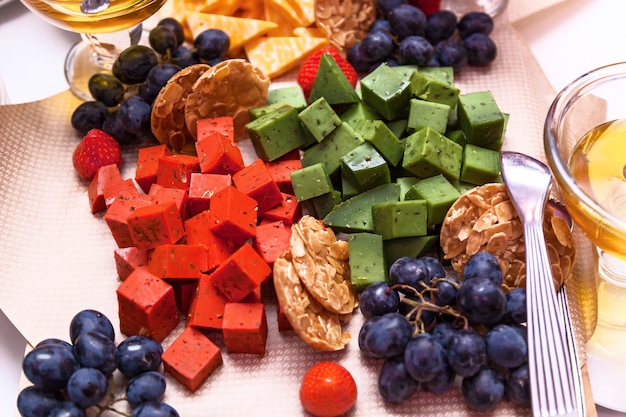 Cubes of red, green cheese with fruits on the table