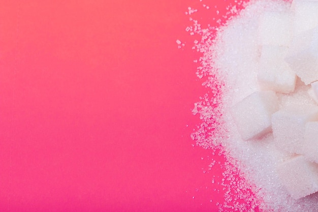 Cubes of white sugar and granulated sugar on an pink background