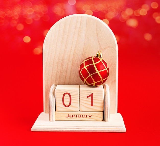 Cubic wooden calendar with the date January 1 and decoration on a red background The concept of a happy New year