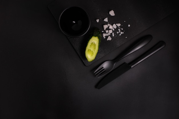 Cucumber on a black background with black cutlery, top view