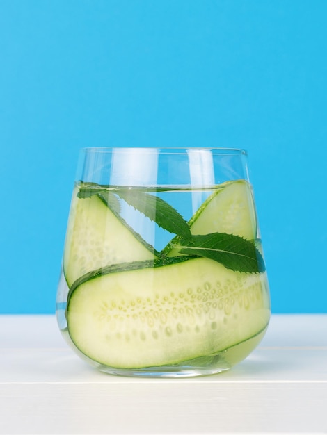 Cucumber slices in a glass glass with water on a white wooden table