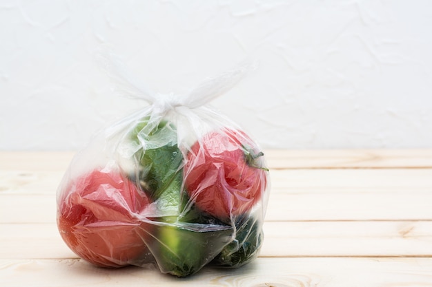 Cucumbers and tomatoes are packed in a disposable plastic bag on a wooden table