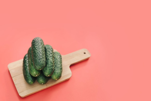 Cucumbers on a wooden board on a pink background