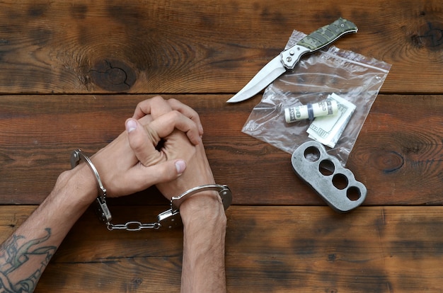 Photo cuffed hands of tattooed criminal suspect and plastic ziplock packet of evidence for investigation