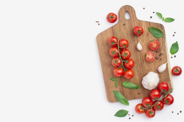 Culinaire achtergrond met houten snijplank cherry tomaten knoflook en basilicum op een wit
