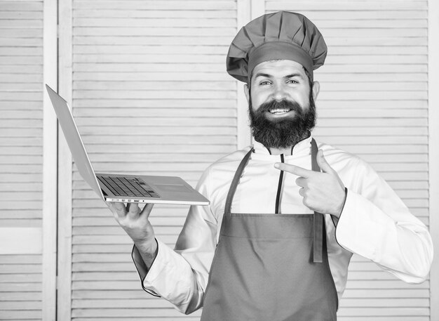 Culinaire school Hipster in hoed en schort producten online kopen Online winkelen Bezorgservice Man chef zoekt online ingrediënten koken eten Kruidenier online Chef laptop bij keuken