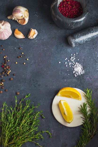 Culinary background. set of different spices, herbs lemon, salt, thyme, pink pepper, rosemary, garlic. on black stone background. Flatlay with copy space. Template food blog social media.