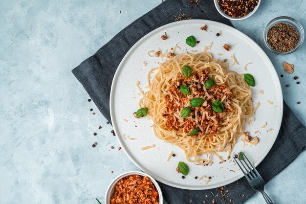 Sfondo culinario con pasta alla bolognese, basilico, formaggio e noci su un tovagliolo scuro su un grigio