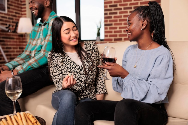 Cultureel diverse nationaliteiten, etniciteiten vrouwen paar chatten, praten, gelukkig discussiëren tijdens het verzamelen van huisvrienden, wijn drinken, broodstengels eten, kaas.