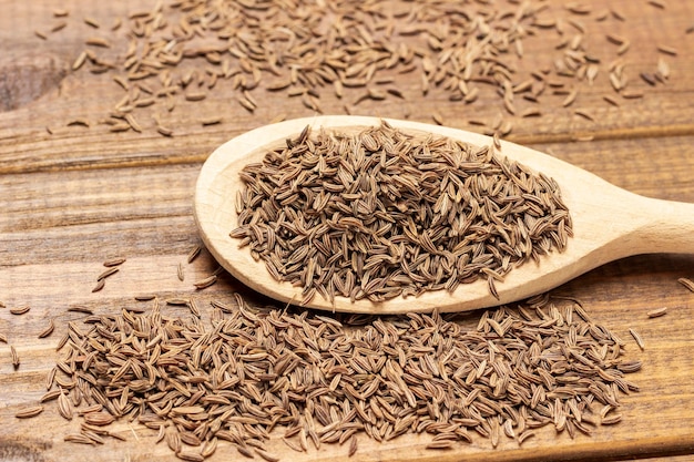 Cumin seeds in wooden spoon Close up Top view Wooden background