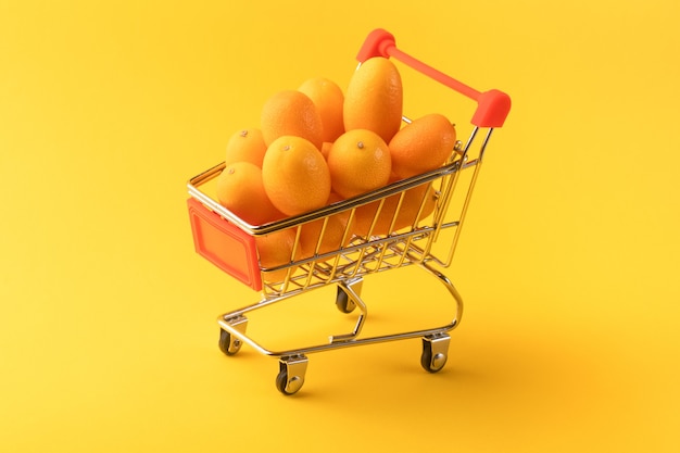 Cumquat of kumquat in een winkelwagentje op gele achtergrond, fruit shopping concept