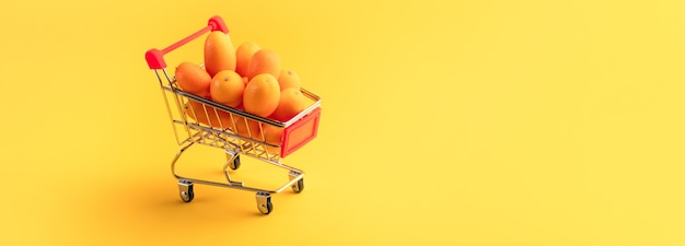 黄色の背景、フルーツショッピングコンセプトのショッピングカート内のキンカンまたはキンカン