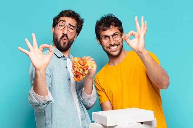 Cuople of two hispanic friends with happy expression and holding take away pizzas