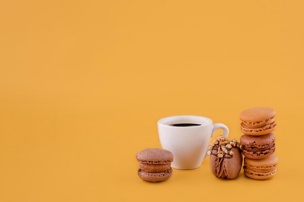 Cup of americano coffee and macaroons on a yellow background Space for text