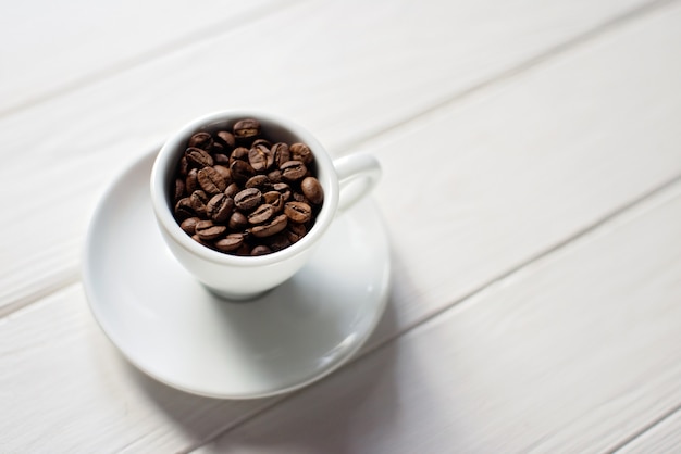 Cup of aromatic coffee beans on a white wooden background