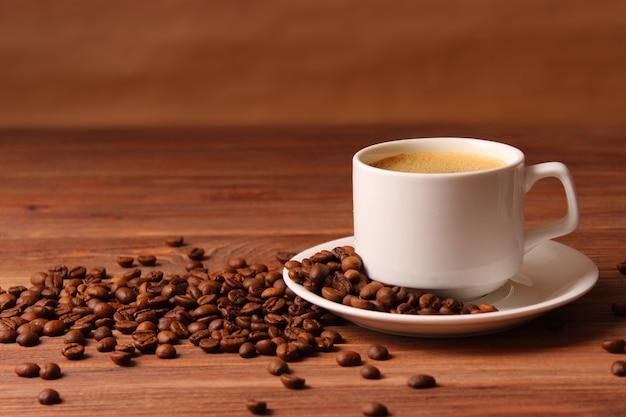 Чашка ароматного кофе и кофейных зерен на деревянном фоне