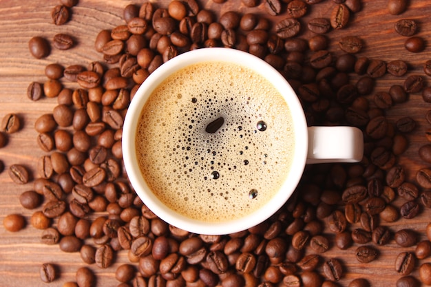 Cup of aromatic coffee and coffee beans on a wooden background