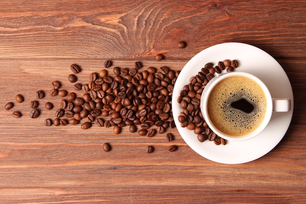 Cup of aromatic coffee and coffee beans on a wooden background