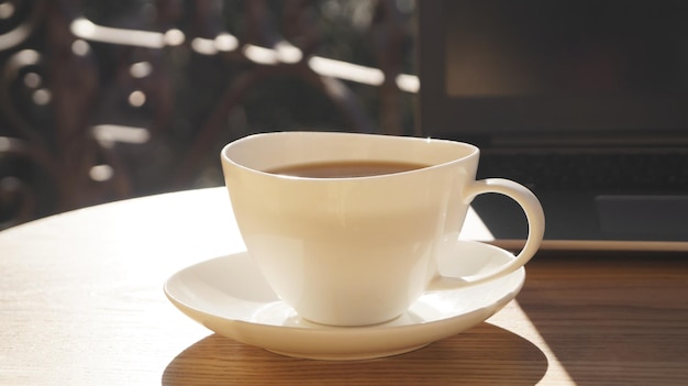 Cup of aromatic coffee and laptop on wooden table outdoors closeup