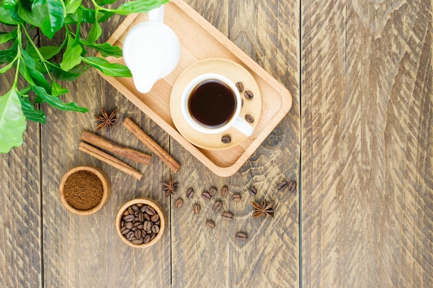 Una tazza di caffè aromatico e un lattaio con il latte su un vassoio. colazione mattutina. foglie di caffè arabica verde su uno sfondo di legno.