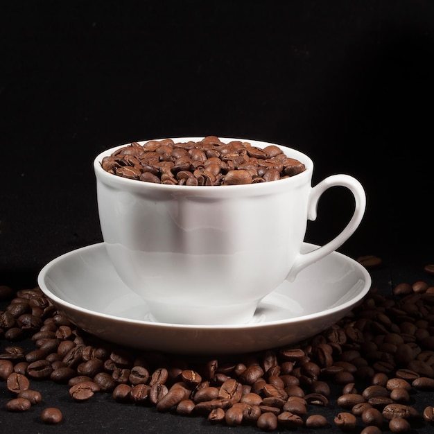 Cup of aromatic coffee with coffee beans on a dark background