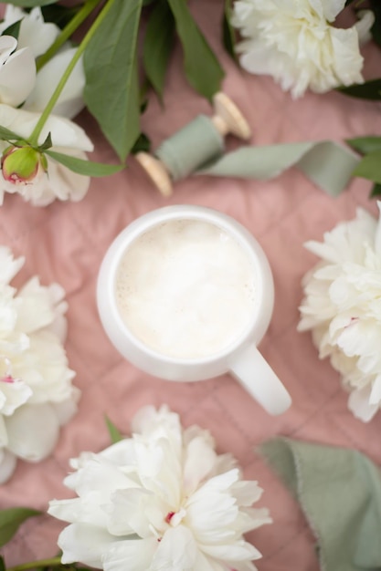 A cup of aromatic delicious coffee in a white cup and peony flowers