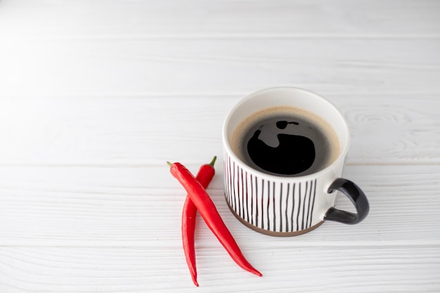 A cup of aromatic hot black coffee on a white background and red acute pepper