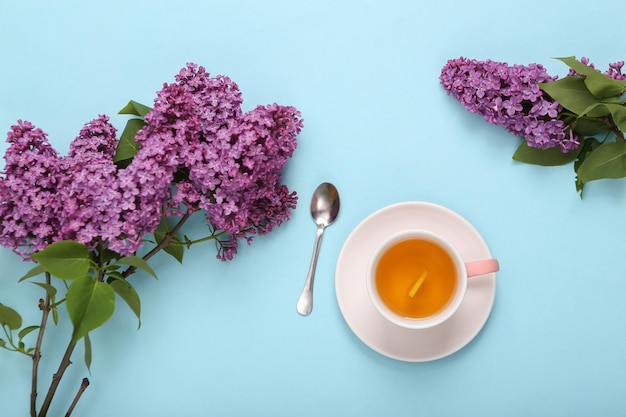 Cup of black aromatic tea with lemon and branches of blooming lilacs on blue pastel background Top view Flat lay